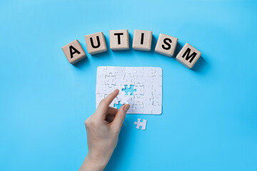 Word Autism made of wooden cubes. Woman solving puzzle on light blue background, top view