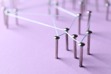 Network connection. Nails linked together by thread on violet background, closeup. Space for text