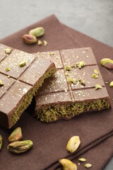 Pieces of tasty Dubai chocolate with pistachios and knafeh on grey table, closeup