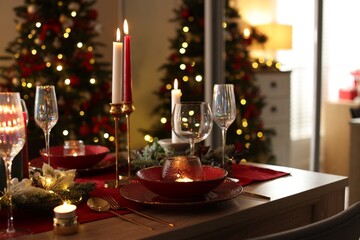 Christmas table setting with stylish dishware, glasses and burning candles in festive decorated room