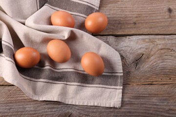 Many fresh eggs and towel on wooden table, flat lay. Space for text