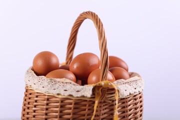 Wicker basket with fresh eggs on white background, closeup