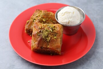 Tasty baklava with chopped nuts and scoop of ice cream on grey table, closeup