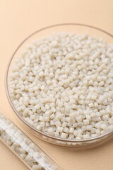 Plastic granules in petri dish and test tube on beige background, closeup