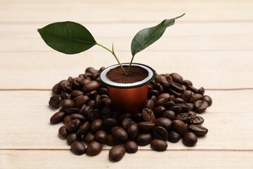 Coffee capsule with seedling and beans on light wooden table, closeup