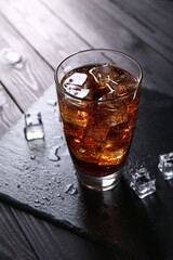 Sweet soda water in glass with ice cubes on black wooden table