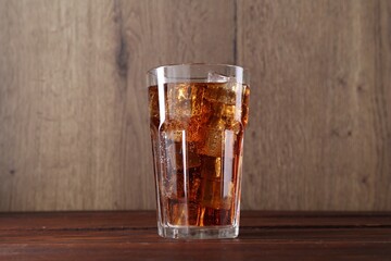 Sweet soda water with ice cubes in glass on wooden table