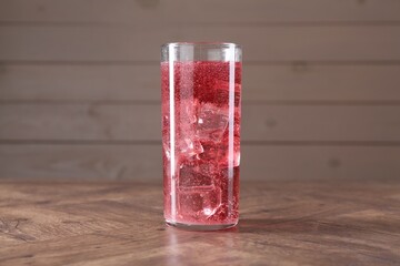 Sweet soda water with ice cubes in glass on wooden table
