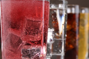 Refreshing soda water of different flavors with ice cubes in glasses, closeup