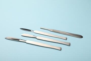 Different surgical scalpels on light blue background, closeup