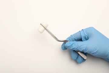 Doctor holding surgical tweezers with gauze on light background, top view. Space for text