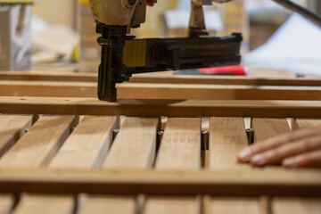 The process of assembling a wooden structure close-up using a construction stapler. Smooth wooden planks placed on the table, as well as the hands of the master.