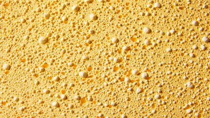 Close-up of a bubbly, yellow surface, showcasing numerous small bubbles against a textured background, creating a vibrant and dynamic visual effect.