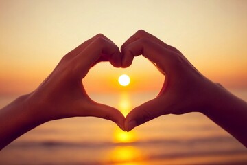 two hands making a heart shape with their fingers. The hands are positioned in front of a beautiful sunset over the ocean.