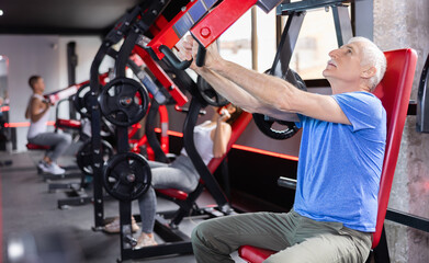 Elderly man in sportswear training her arms on machine in gym