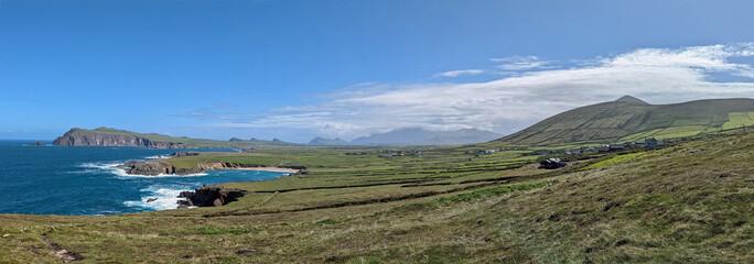 Panoramic view under blue cloudy sky over the green meadows of west Ireland in County Kerry overlooking Clogher beach