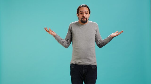 Man shrugging shoulders, unable to provide answer, having detached apathy facial expression. Apathetic person doing hand gesturing showing lack of knowledge, studio background, camera A