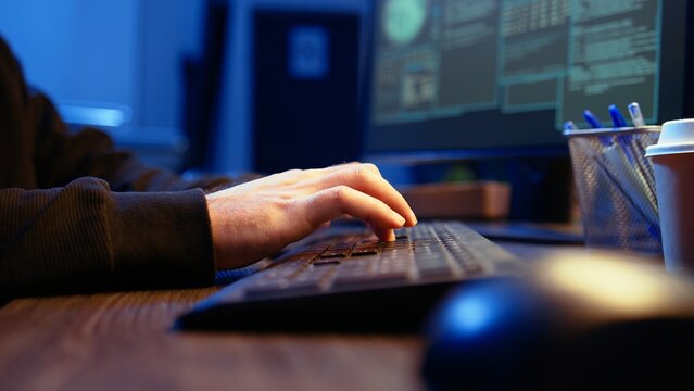 Hacker in secret underground shelter typing on keyboard, writing lines of code on computer, trying to get past security systems with virus. Scammer working on hacking script, camera A close up shot