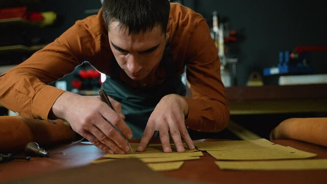 Craftsman intently tracing patterns onto leather sheets, showcasing precision and craftsmanship in the early stages of leather goods creation