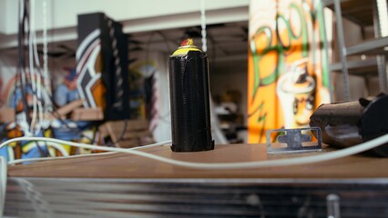 Close up of spray cans in empty basement with graffiti drawings on walls. Focus on paint cans with underground warehouse used as crime haven by hooligans in blurry background