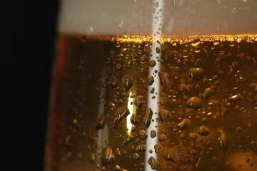Glass of beer with condensation drops on black background, macro view