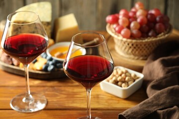 Red wine and different snacks served on wooden table, closeup