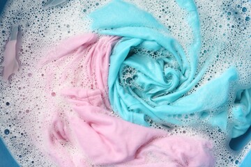Colorful clothes soaked in water before washing, top view
