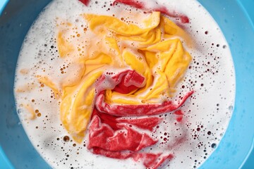 Colorful clothes soaked in water before washing, top view