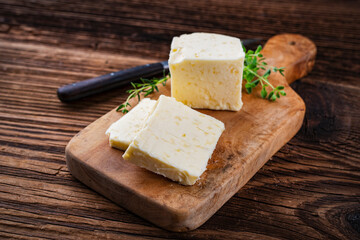 Fresh French sea salt butter garnished with thyme offered as close-up on a rustic wooden chopping board