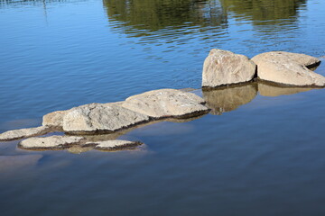 Craftly placed divider rocks at the edge of recreational Cortez park lake with reflecting tree crowns in the distance