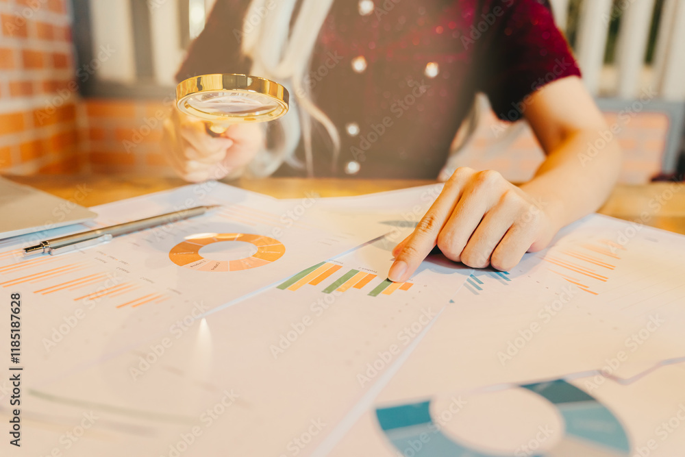 Poster person analyzing data with magnifying glass over printed graphs and charts