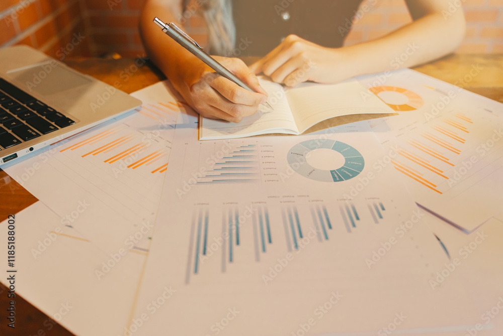 Poster person writing notes on notepad with business graphs and laptop on table