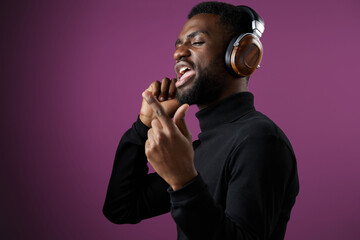 A young Black male enjoying music while singing passionately, wearing stylish headphones, against a vibrant purple background, showcasing a joyful and energetic vibe