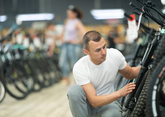 Experienced cyclist expertly examining wheel while selecting new comfortable and reliable bicycle for traveling and bikepacking in specialized bike shop