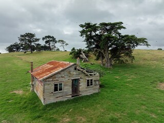 Abandoned weathered farmhouse on a grassy hill under a cloudy sky. Ruined structure, rustic charm.  TE KOPURU, NORTHLAND, NEW ZEALAND
