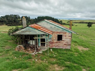 Abandoned weathered house on a grassy field. Ruined structure, overgrown with nature. Empty, decaying home.  TE KOPURU, NORTHLAND, NEW ZEALAND