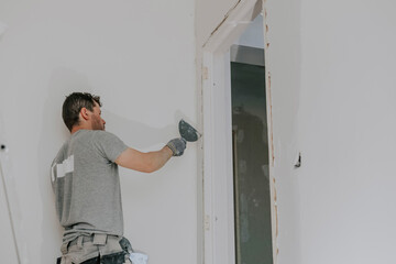 A young builder is plastering a doorway.