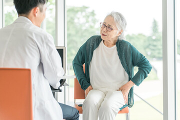 股関節の痛みを訴える高齢者女性と診察する男性医師の後ろ姿
