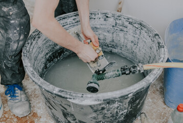 A young builder washes spatulas in a basin.