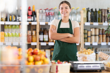 Young female seller in apron standing at counter in grocery store
