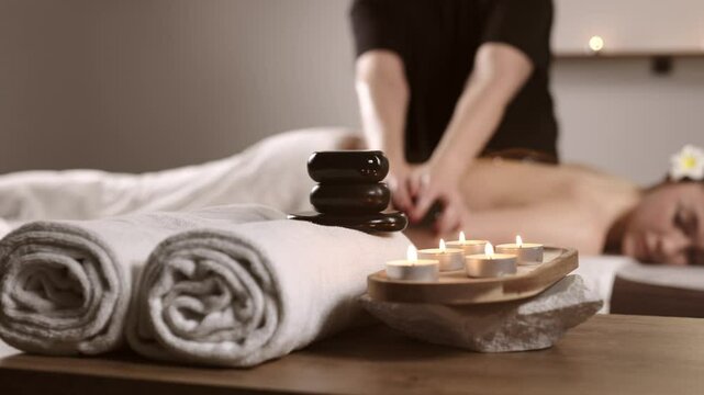 Hot stone massage in a candlelit spa. A blissful woman enjoys the soothing warmth of basalt stones gliding over her body.