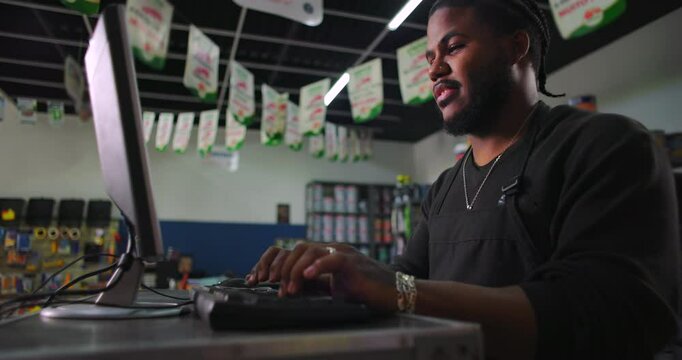 Young man at a computer in a paint store, focused on inventory management and customer service, representing retail work and modern technology