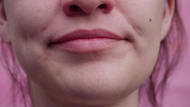 Close-up of a woman yawning, revealing teeth, gums, and tongue against a contrasting soft pink background.