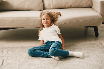 Little girl with windblown hair sitting on the floor in front of a cozy couch in a sunlit room