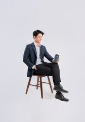 Full body image of young Asian business man sitting in chair and drink coffee on white background