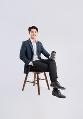 Full body image of young Asian business man sitting in chair and drink coffee on white background