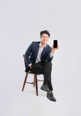 Full body image of young Asian business man using phone and sitting in chair on white background