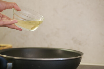 Carefully pouring cooking oil into a pan as part of the preparation process