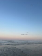 Calm beach ocean waves at sunset, with a view of the moon