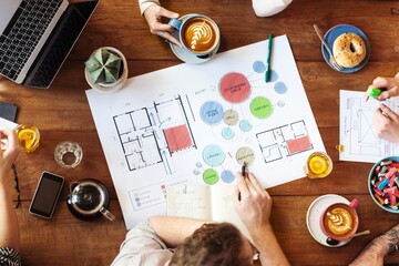 Team collaborates on architectural plans. Diverse group discusses design, strategy, and innovation. Creative workspace with coffee and snacks. Planning and teamwork. Arcitechture plan on coffee table